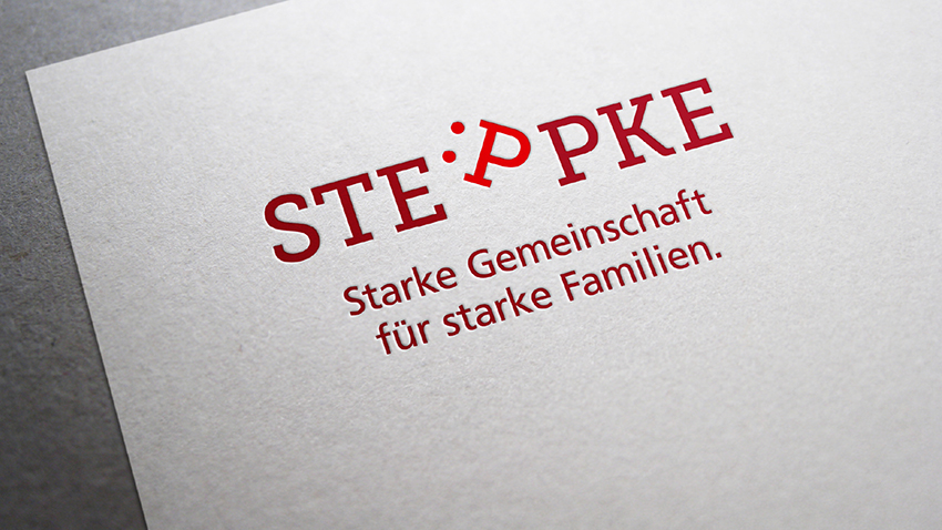 Ein weißes Blatt Papier mit dem roten STEPPKE-Logo, bei dem das zweite „P“ als Smiley-Gesicht stilisiert ist, und darunter steht der Slogan „Starke Gemeinschaft für starke Familien“.