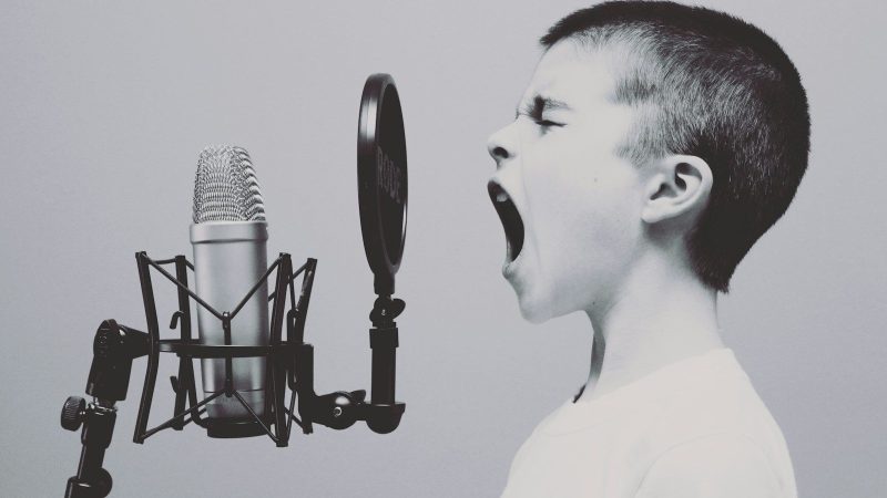 Junge ca. 10 Jahre singt an einem retro Mikrophon, Bild ist schwarz weiß