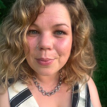 Ein Portrait Foto von Mira Herhammer mit Nahaufnahme vom Gesicht vor grünem Natur Hintergrund. Mira hat blonde locken.